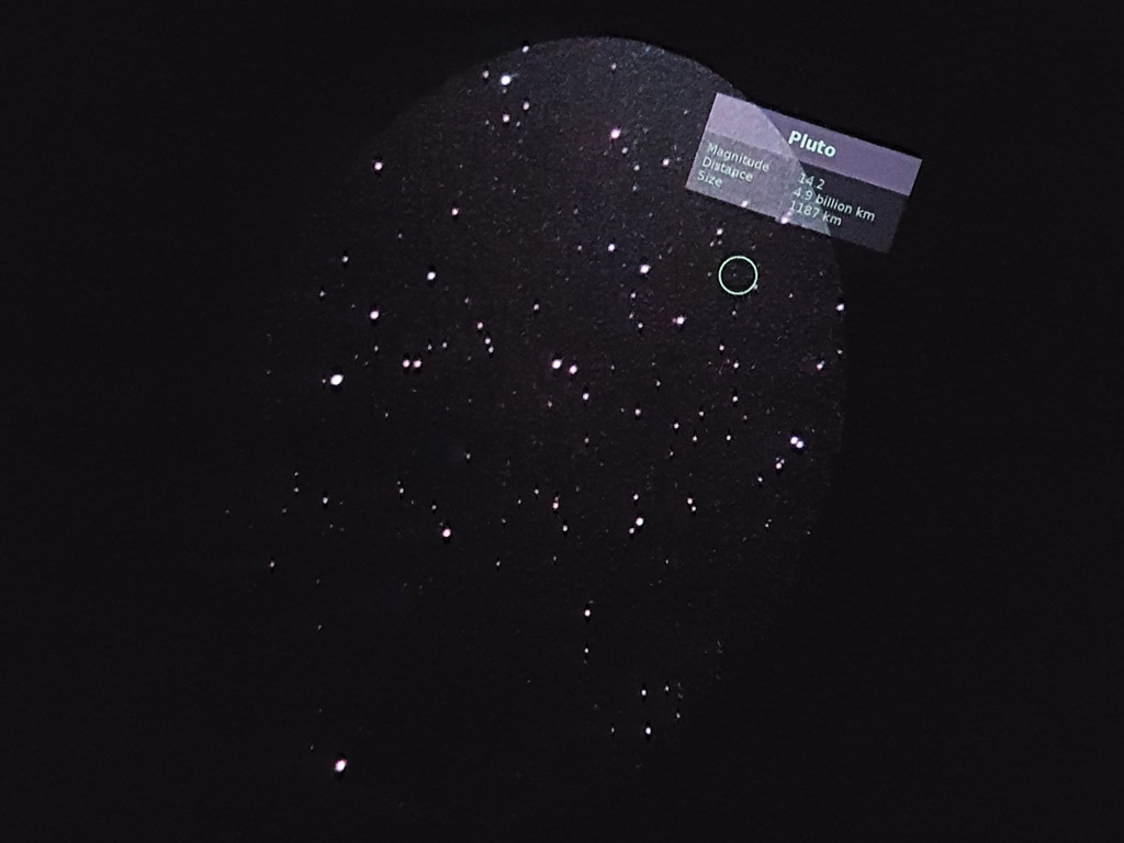 Picture taken with a cellphone in the eyepiece of the telescope. The green circle labels the position of Pluto, which is visible.